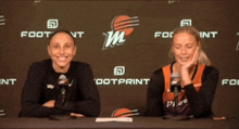 two women are sitting at a table in front of a wall that says footprint on it