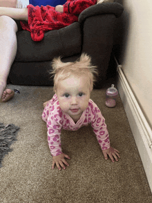 a baby is crawling on the floor next to a pink bottle