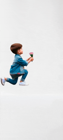 a young boy in a denim jacket is kneeling down holding a bouquet of flowers