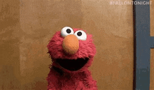 elmo from sesame street is standing in front of a wooden wall and looking at the camera .