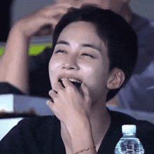 a young man is sitting in a stadium with a bottle of water and laughing .