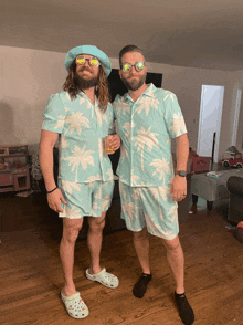 two men wearing palm tree shirts and crocs pose for a photo