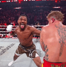 two men are fighting in a boxing ring and one is sticking his tongue out .
