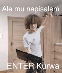 a man with curly hair is holding a laptop in front of a wooden door with the words enter kurwa below him