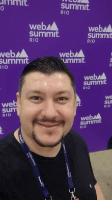 a man is smiling in front of a web summit rio sign