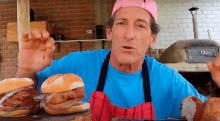 a man wearing a pink hat and apron is standing in front of two hamburgers on a table .