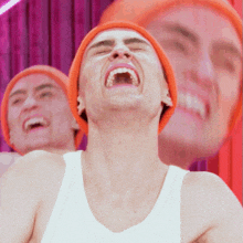 a man wearing an orange beanie and a white tank top laughs