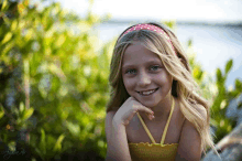 a young girl wearing a yellow top and a red and white headband smiles for the camera