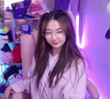 a girl wearing glasses is sitting in a chair in front of a shelf with a twitch logo on it