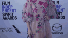 a woman in a floral dress stands in front of a wall that says " film independent spirit awards "