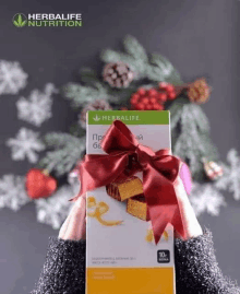 a woman is holding a herbalife box with a red bow