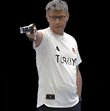 a man wearing a white t-shirt that says turkey is pointing a gun