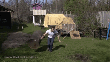 a man in a white shirt is holding a large barrel in a yard with the website www.thehacksmith.ca in the corner