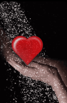 a hand is holding a red heart that is surrounded by glitter