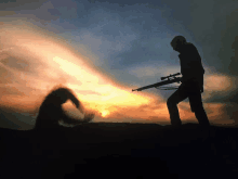 a silhouette of a man holding a rifle against a sunset sky