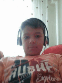 a young boy is wearing headphones and a t-shirt while sitting on a couch .