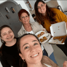 a group of women are posing for a picture and one of them is holding a box of food