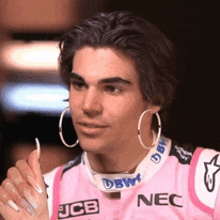 a man wearing hoop earrings and a pink jcb nec shirt