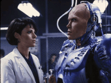 a woman in a lab coat stands next to a man in a robot suit