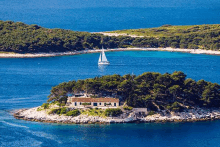 a small island in the middle of a body of water with a sailboat in the distance .