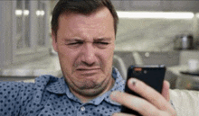 a man is making a sad face while looking at his cell phone .