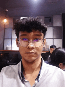 a man wearing glasses and a shirt with the letter p on it looks at the camera