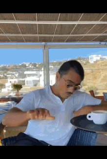 a man in a white shirt is sitting at a table with a cup of coffee in front of him .