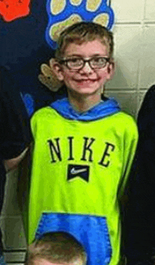 a young boy wearing glasses and a neon green nike hoodie is standing next to a group of children .