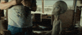a man in a blue shirt is standing next to a small grey alien