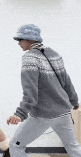 a man wearing a hat and a grey sweater is walking