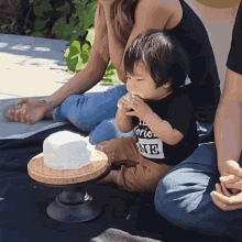 a little boy wearing a shirt that says " i 'm one " is sitting on the ground eating a cake