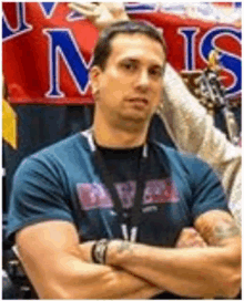 a man in a blue shirt with his arms crossed is standing in front of a sign that says ns .