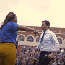 a man in a white shirt and tie stands next to a woman in a blue shirt holding a microphone