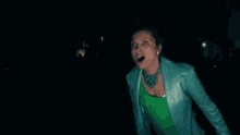 a woman in a green shirt and a blue jacket is standing in the dark