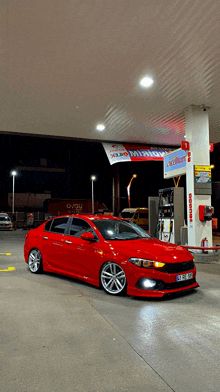 a red car is parked at a gas station with a sign above it that says cadium