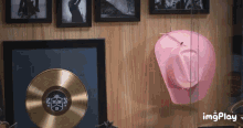 a pink cowboy hat is hanging on a wooden wall next to a gold record