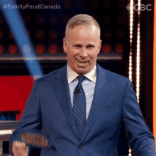 a man in a blue suit and tie is standing in front of a sign that says family feud canada