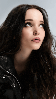 a woman with long dark hair and a black jacket looks up