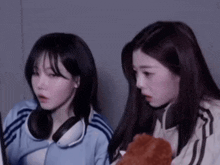 two young women are sitting next to each other and looking at something . one of the girls is wearing headphones .