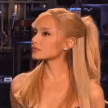 ariana grande is wearing a ponytail and earrings while sitting in front of a microphone .