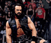 a man with a beard is standing in front of a crowd wearing a leather vest and shorts .