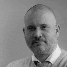 a black and white photo of a bald man with a beard wearing a tie .