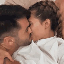 a man and a woman kissing on a bed with the woman wearing a white shirt