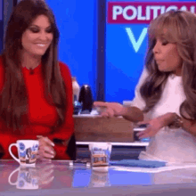 two women are sitting at a table with a sign that says political