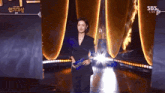 a woman in a black suit is standing in front of a sbs live banner