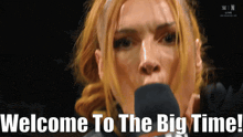 a woman speaking into a microphone with the words welcome to the big time written below her