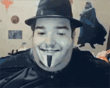 a man wearing a hat and a v for vendetta mask is smiling at the camera .