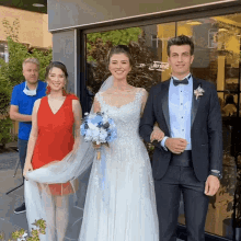 a man in a blue shirt stands behind a woman in a red dress and a man in a black tuxedo