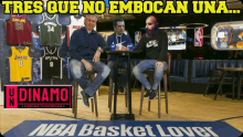 three men sit at a table in front of a nba basket lover sign