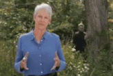 a woman in a blue shirt is standing in front of a tree holding a bird .